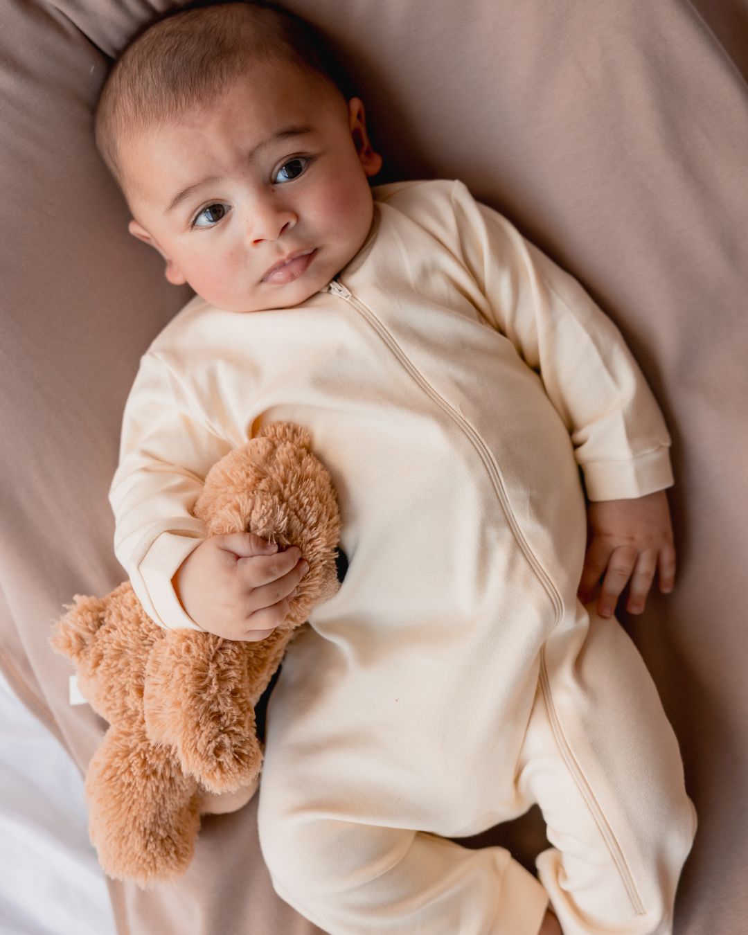 Baby holding a teddy bear in the natural zipper sleepsuit