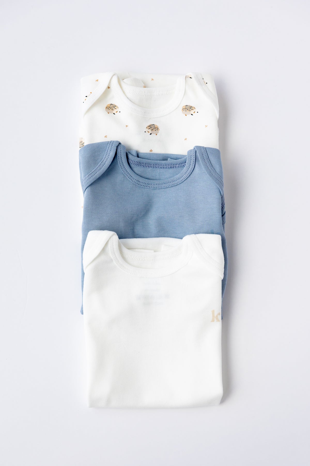 Three short sleeve bodysuits in dusty blue, white and Hedgehog Meadow print
