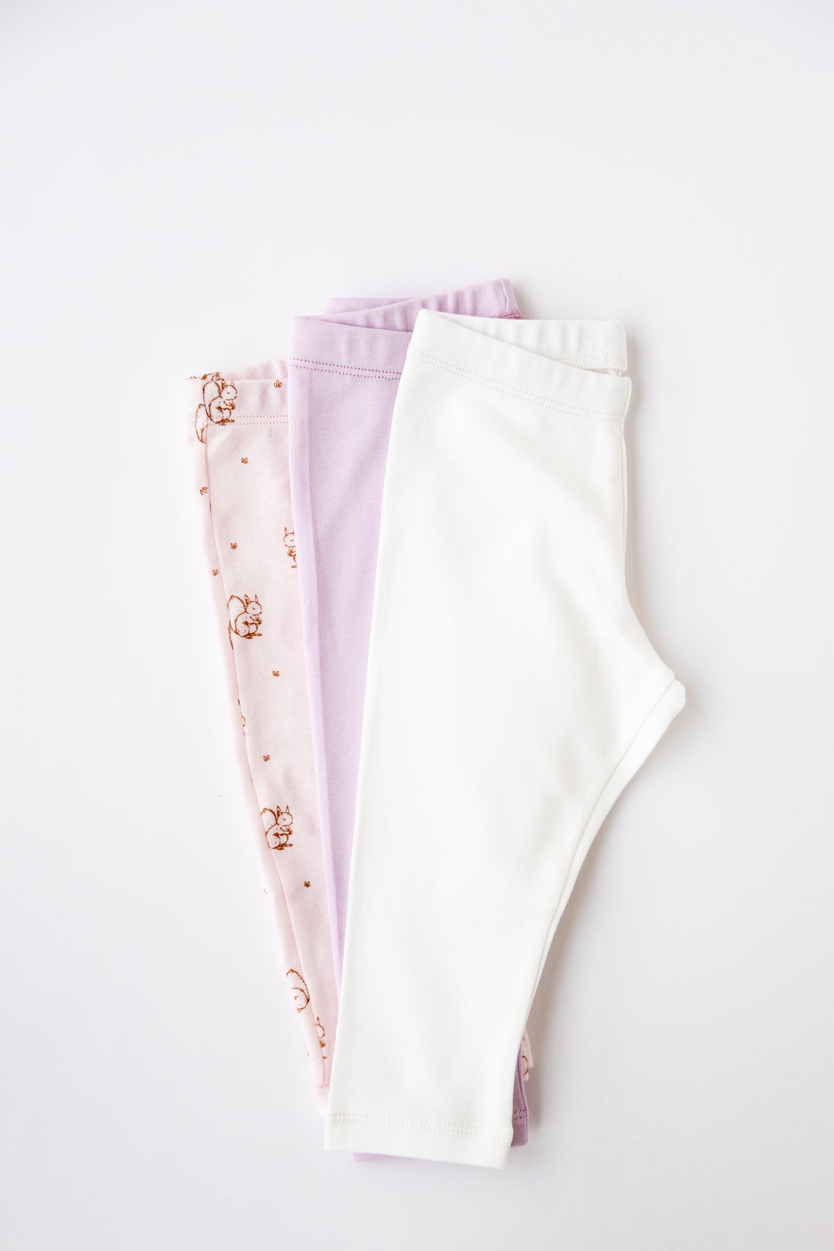 Three pairs of baby leggings in soft pastel shades, laid flat