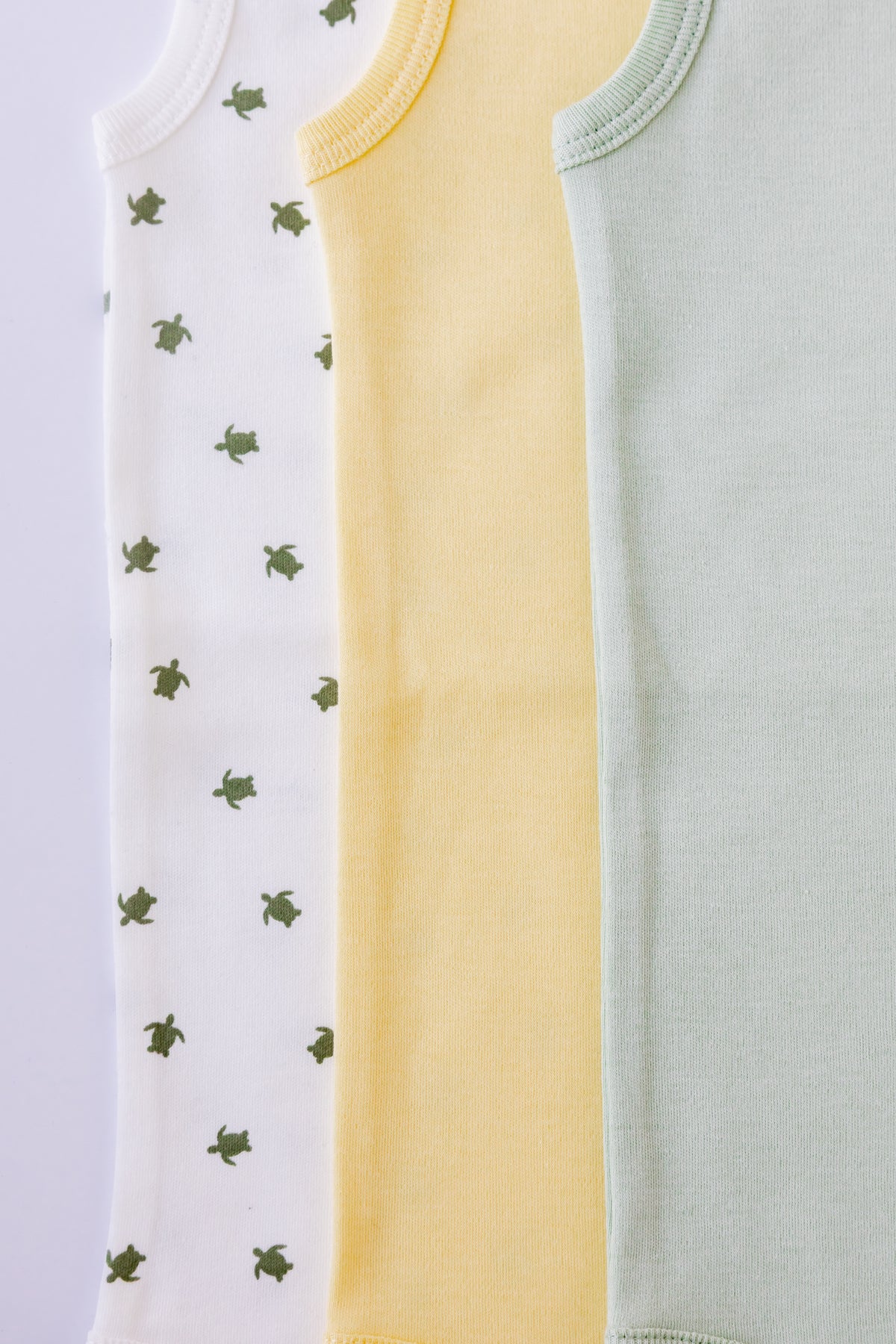 Turtle Bay print sleeveless bodysuit laid flat beside a butter yellow pair