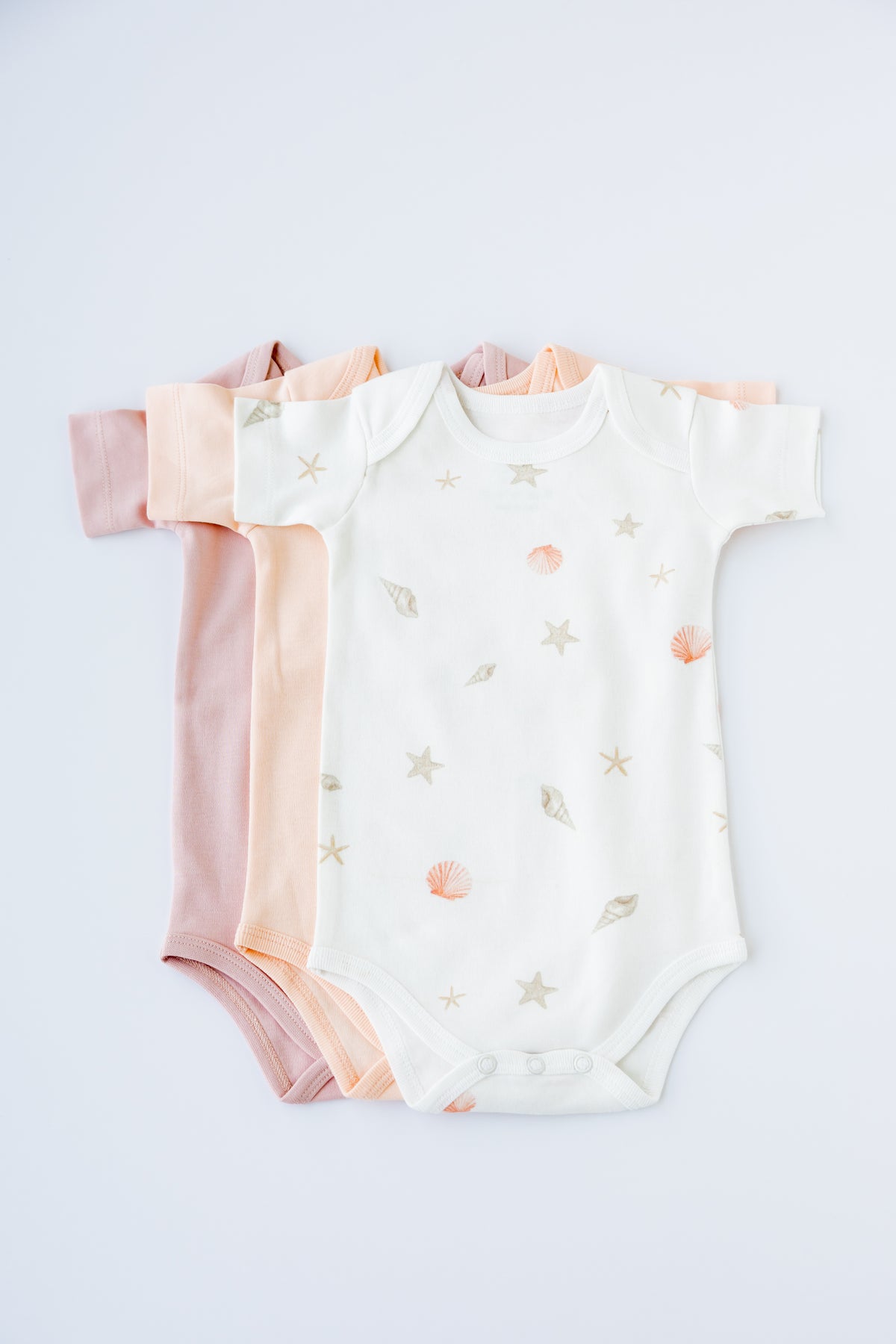 Three short sleeve bodysuits in blush, white and Seashell print