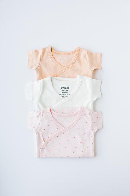 Tiny Love kimono bodysuits folded and stacked in coral and blush
