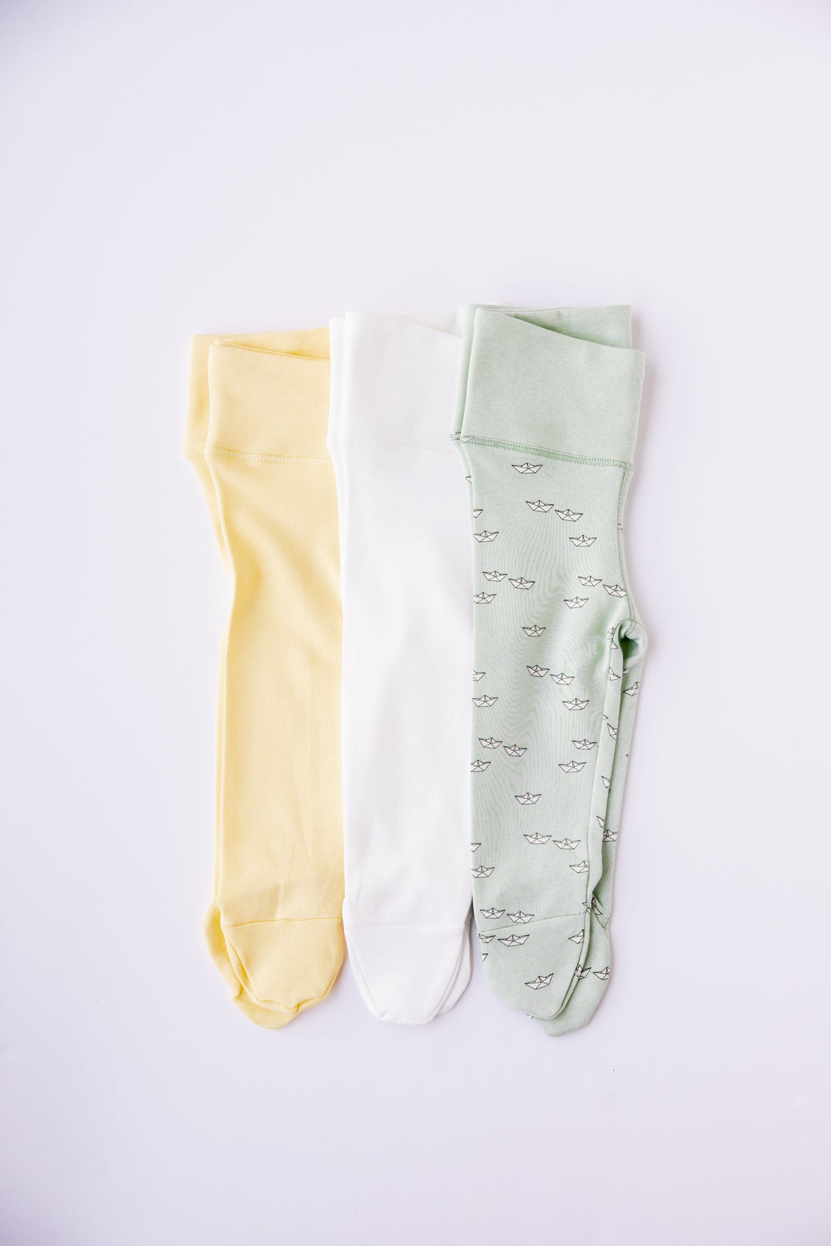 Three pairs of footed leggings in butter yellow, sage and Paper Boats print