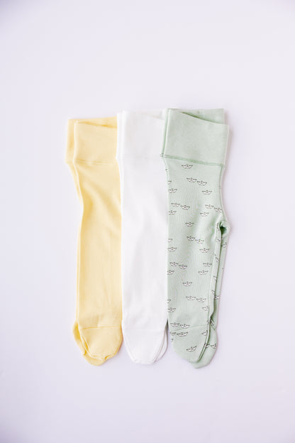 Three pairs of footed leggings in butter yellow, sage and Paper Boats print