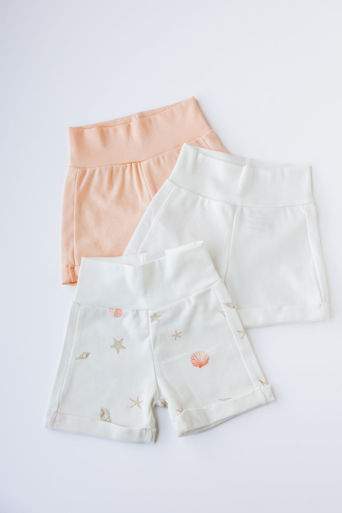 Three pairs of baby shorts in peach, white and Sea Shells print