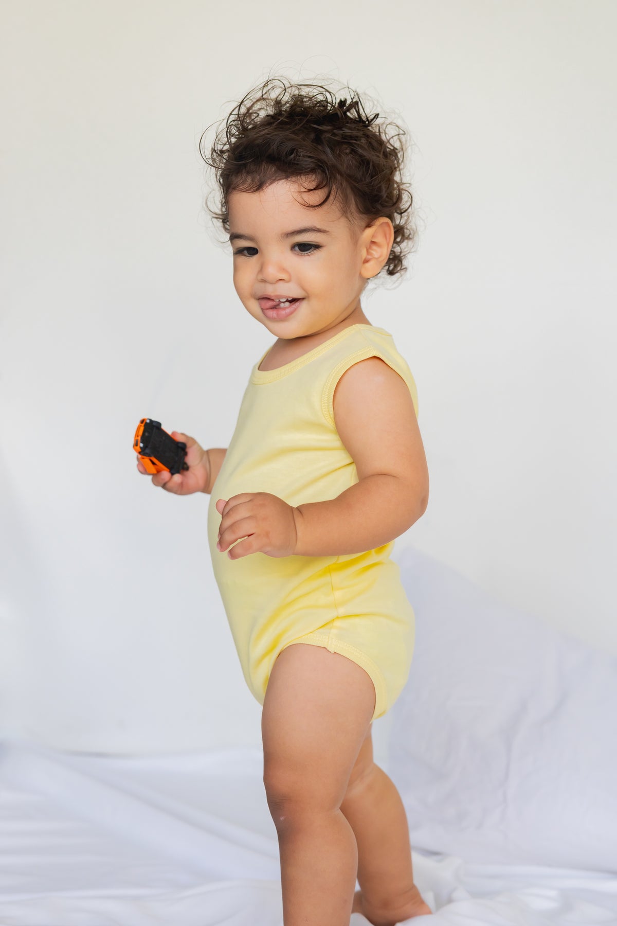 Toddler standing in a butter yellow sleeveless bodysuit