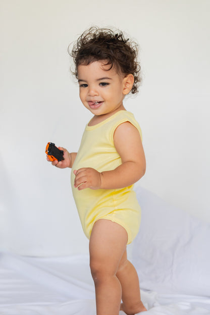 Toddler standing in a butter yellow sleeveless bodysuit