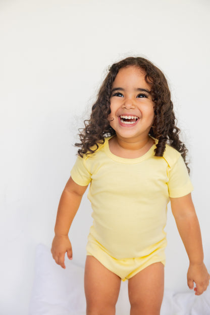 Toddler standing in a butter yellow short sleeve bodysuit