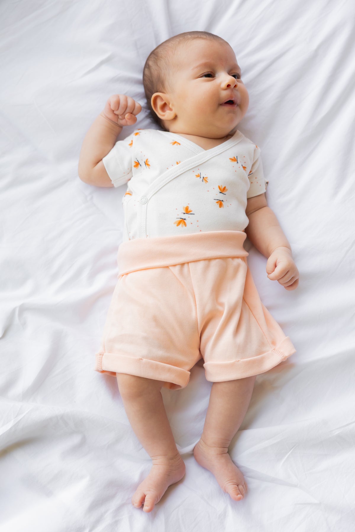 Baby lying down in the Dainty Wings kimono bodysuit and coral shorts
