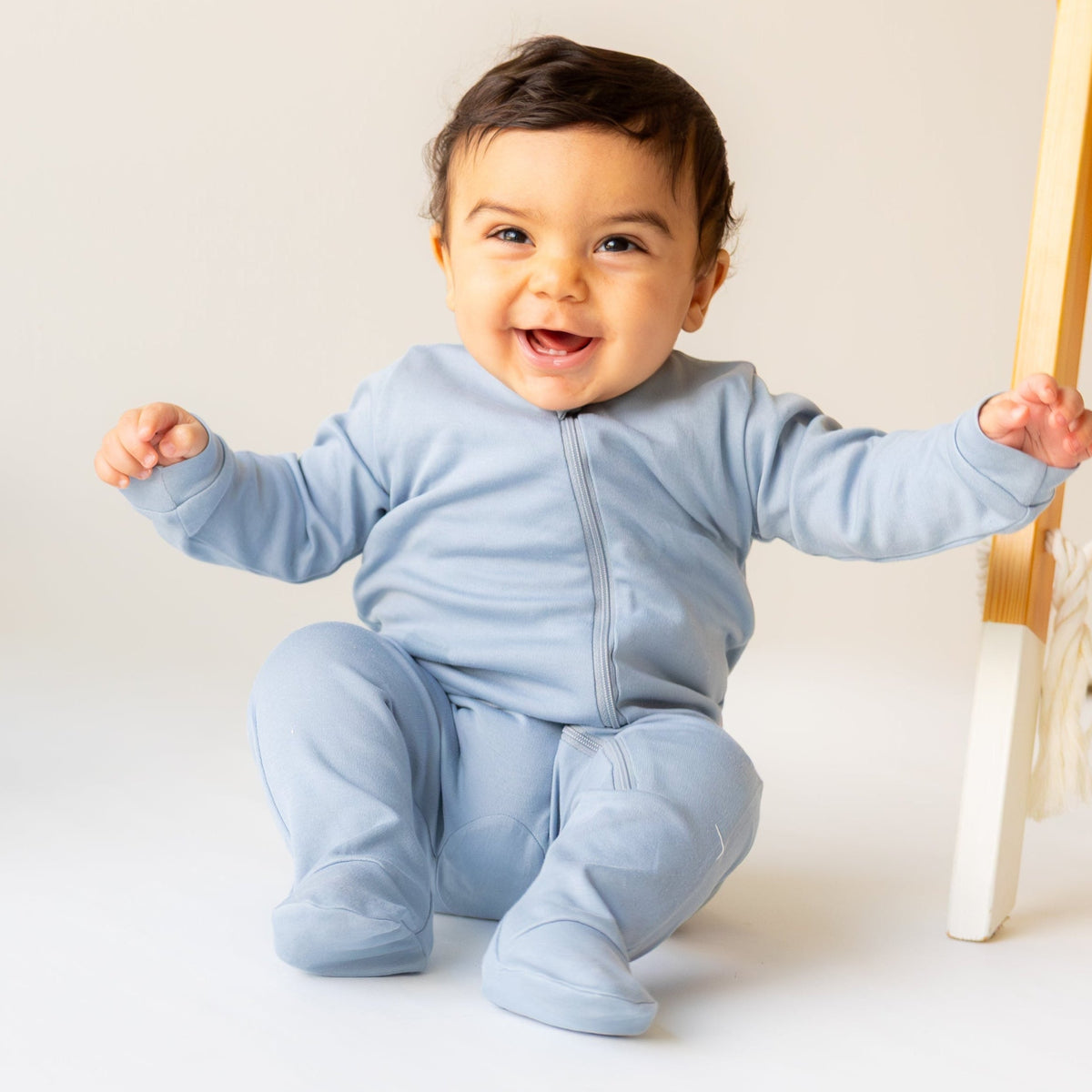 Smiling baby standing in the dusty blue two-way zipper sleepsuit