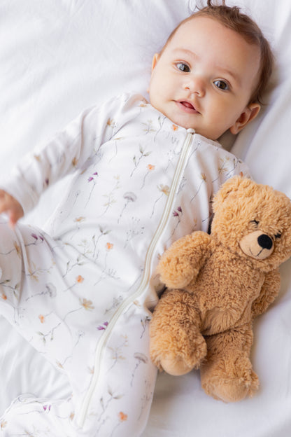 Baby beside a teddy bear in the Wildflower footed zipper sleepsuit