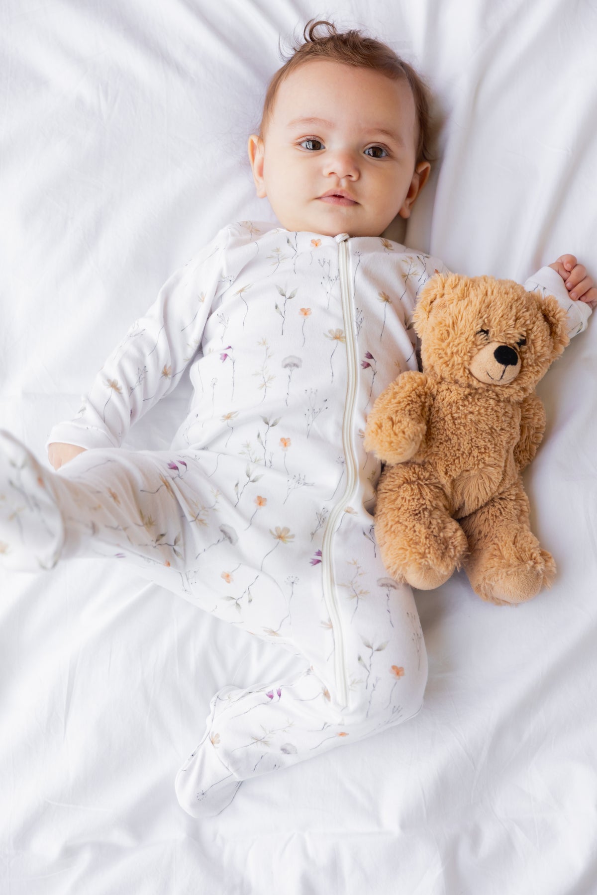 Baby lying with a teddy in the Wildflower print footed sleepsuit