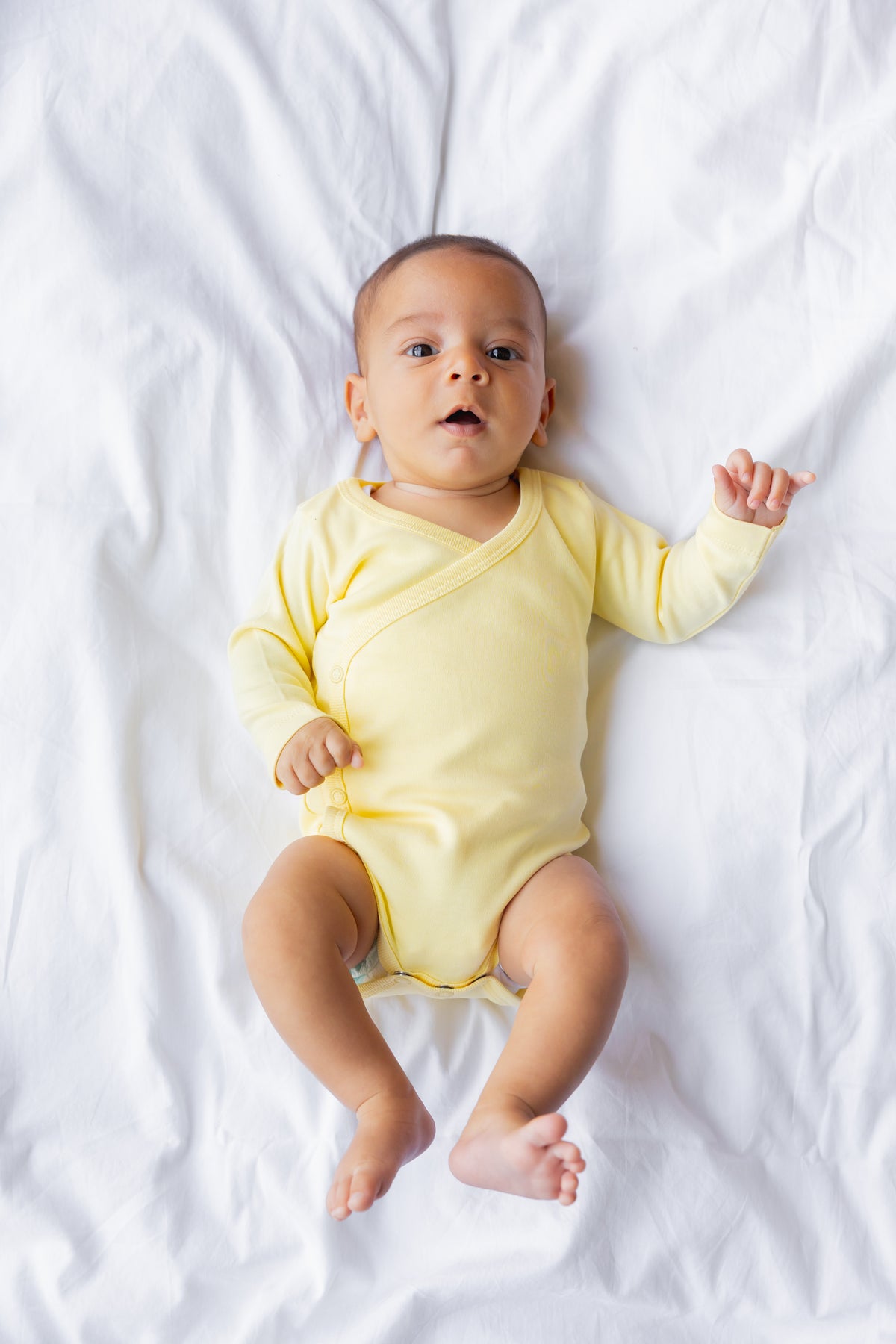 Baby lying down in a butter yellow kimono bodysuit