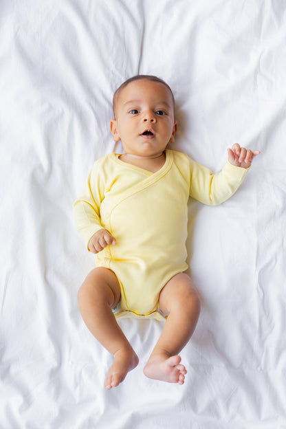 Baby lying down in a butter yellow kimono bodysuit