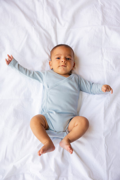 Baby lying down with arms out in a sky blue kimono bodysuit