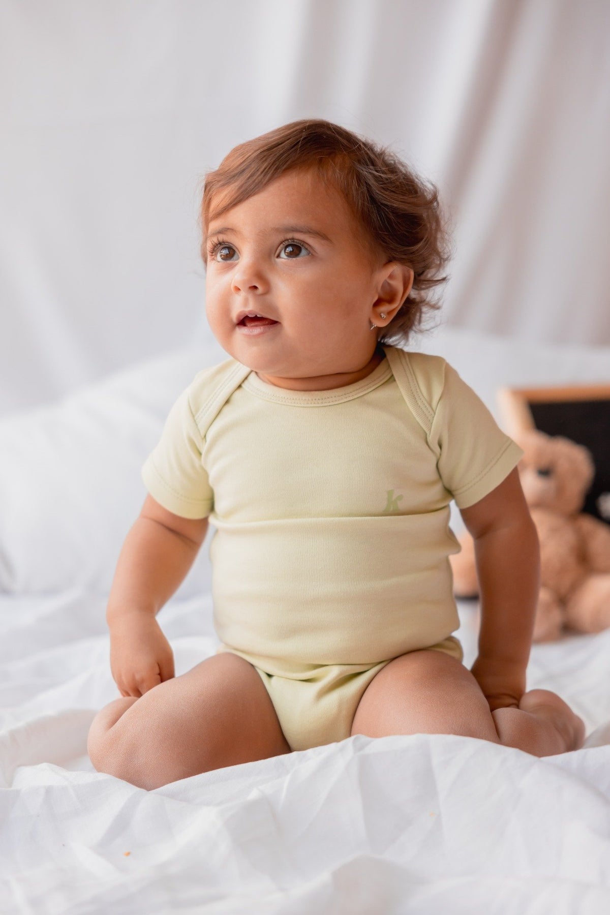 Baby sitting in a pale yellow short sleeve bodysuit