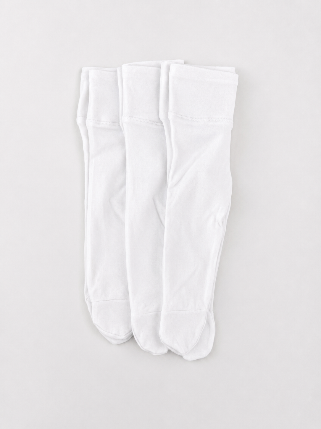 Three pairs of white footed leggings, laid flat
