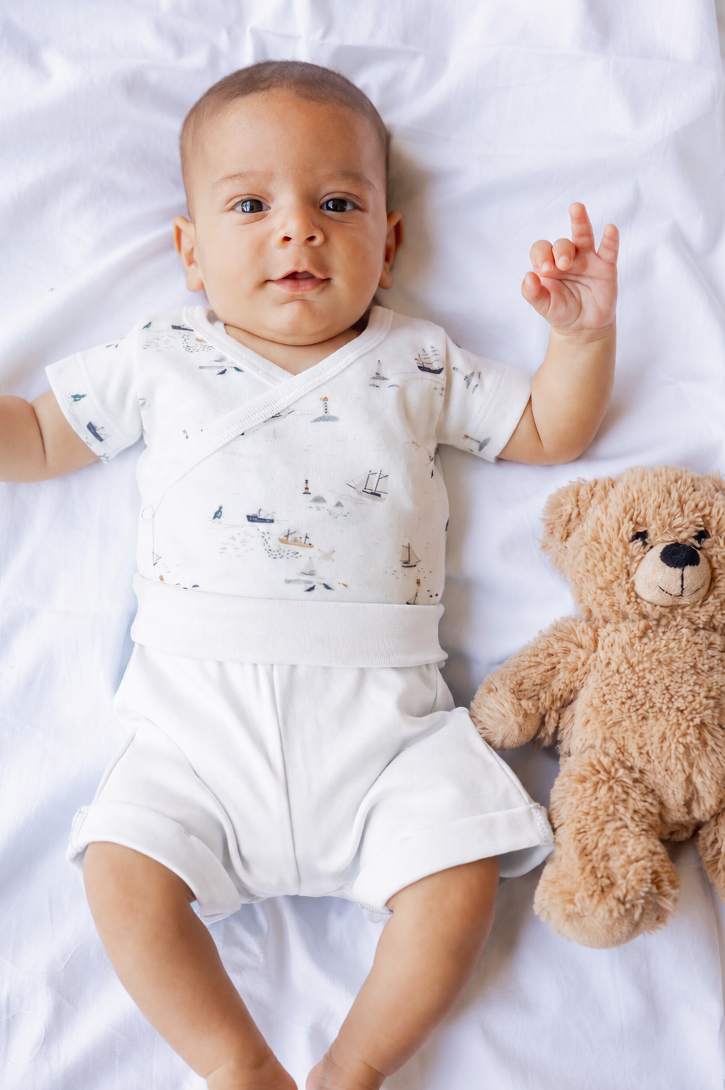 Baby lying down with a teddy, wearing the Little Voyage kimono bodysuit and shorts