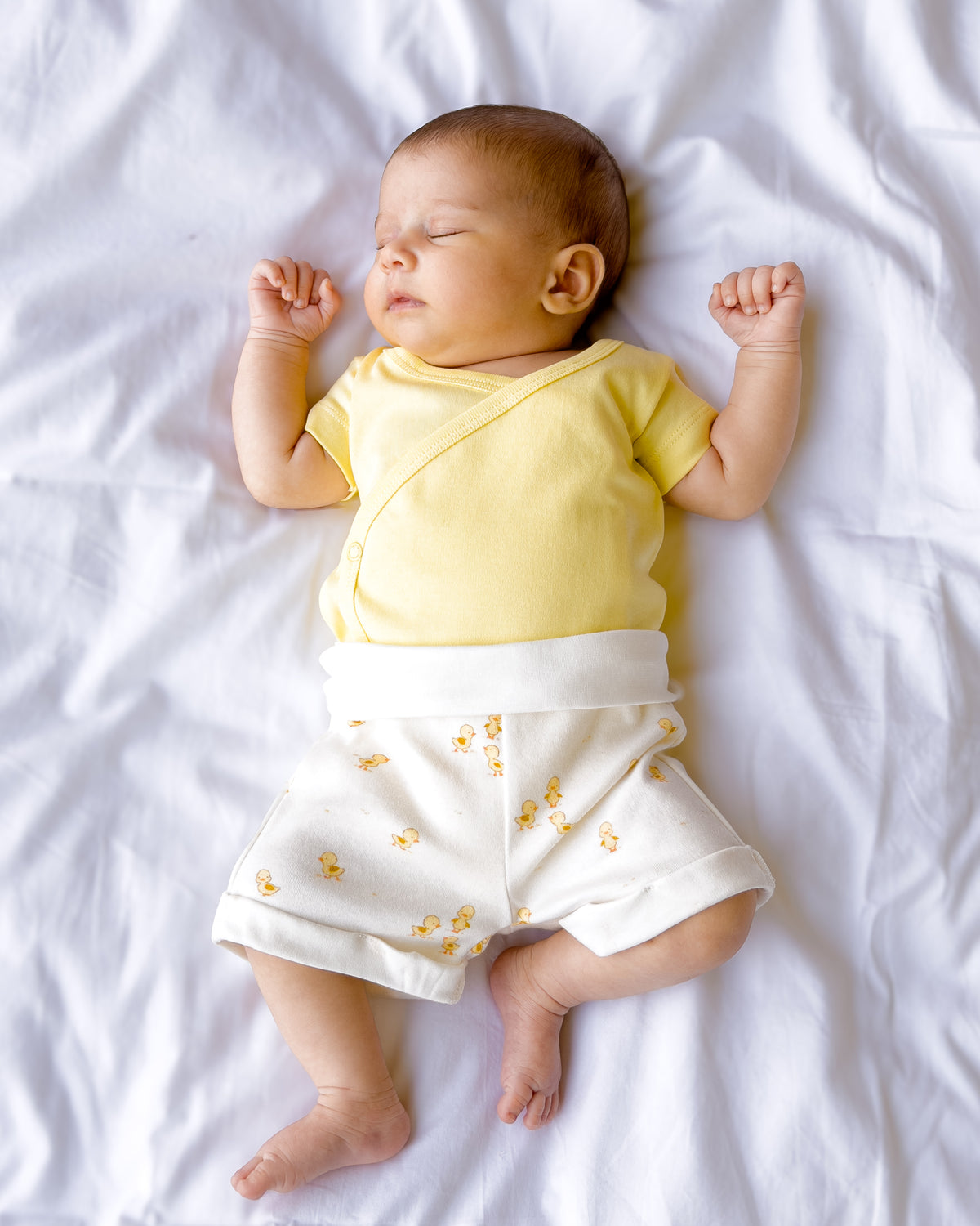 Baby lying down in a butter yellow kimono bodysuit and Ducky Days duck print shorts