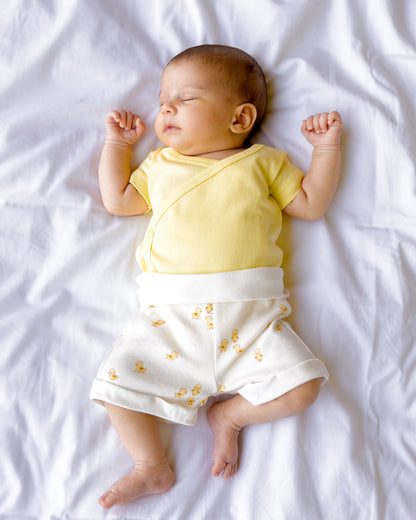 Baby lying down in a butter yellow kimono bodysuit and Ducky Days duck print shorts