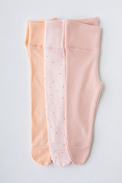 Three pairs of footed leggings in coral, cashmere and Tiny Hearts print